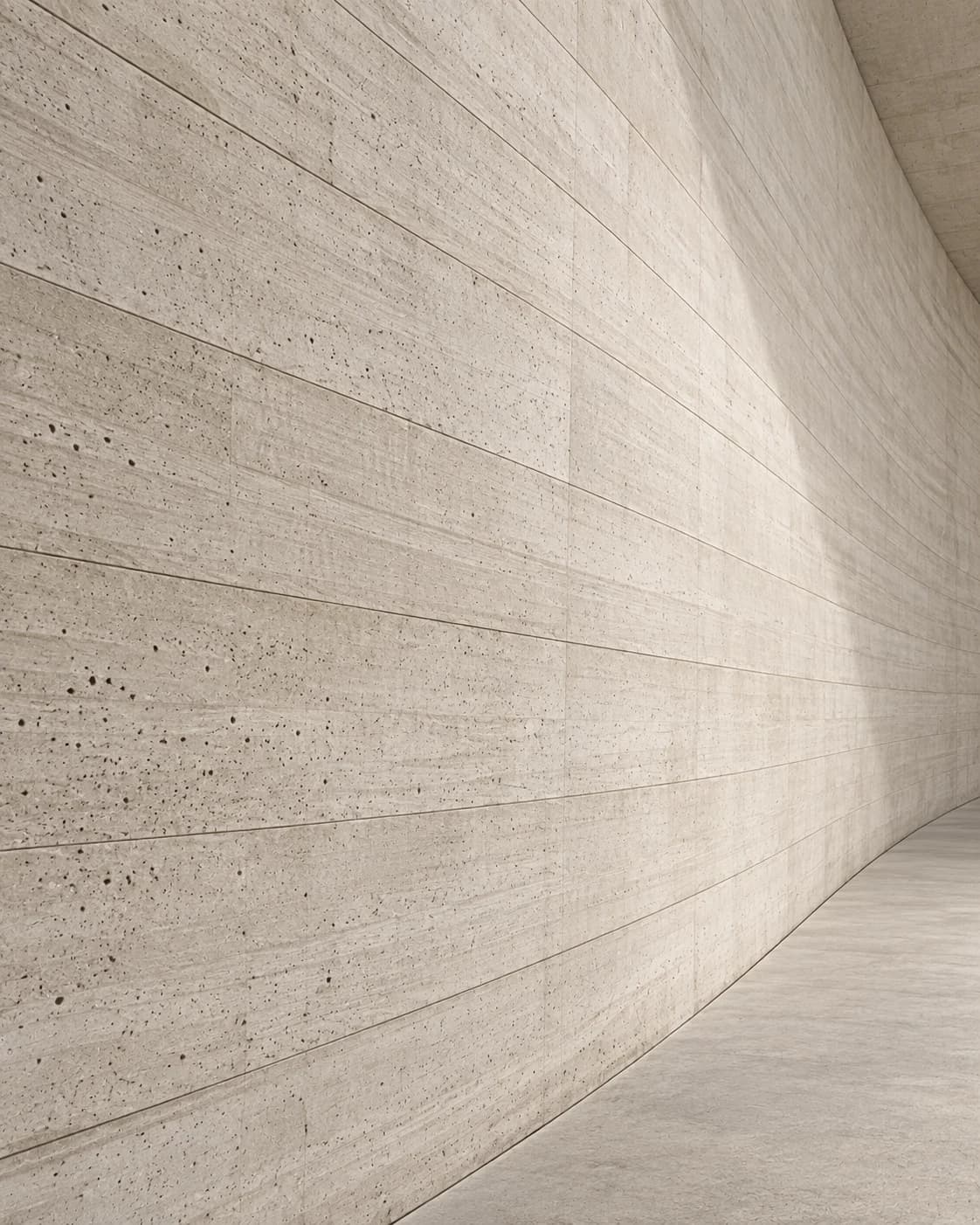 Abstract view of a curved concrete wall receding, raking light along its form-work lines.